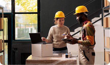 Two people in hard hats collaborate in front of a laptop, likely reviewing construction plans or project details